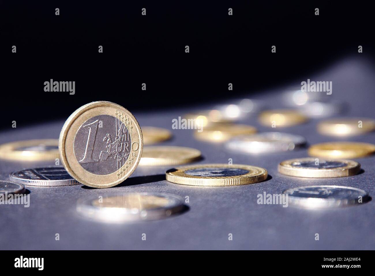 Ein Euro Münze auf der Kante shining in Spotlight, gegen viele verschiedene Münzen auf dunklem Hintergrund. Gelder fließen. Stockfoto