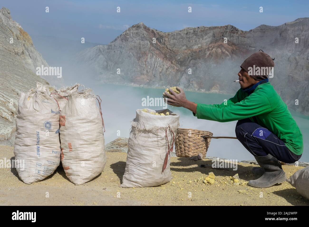 Ein Indonesien Schwefel Miner bricht seine Last von Schwefel in kleinere Stücke, bevor er transportiert es die Ijen Vulkans. Die Ijen Vulkan ist einer der wenigen Orte, an denen Schwefel noch ohne Maschinen abgebaut ist, den Krater des Vulkans hat einen aktiven Schlot produziert, dass elementarer Schwefel. Atmung in den Schwefel Gas kann langfristige gesundheitliche Auswirkungen verursachen, aber trotzdem gibt es keinen Mangel an lokalen Bergleute riskieren alles, was ein gutes Gehalt zu verdienen ist, Bergarbeiter, einem durchschnittlichen Einkommen dreimal höher als die der lokalen Gehalt. Reiner Schwefel ist im Haushalt Reinigung Produkte verwendet, Make up, Explos Stockfoto