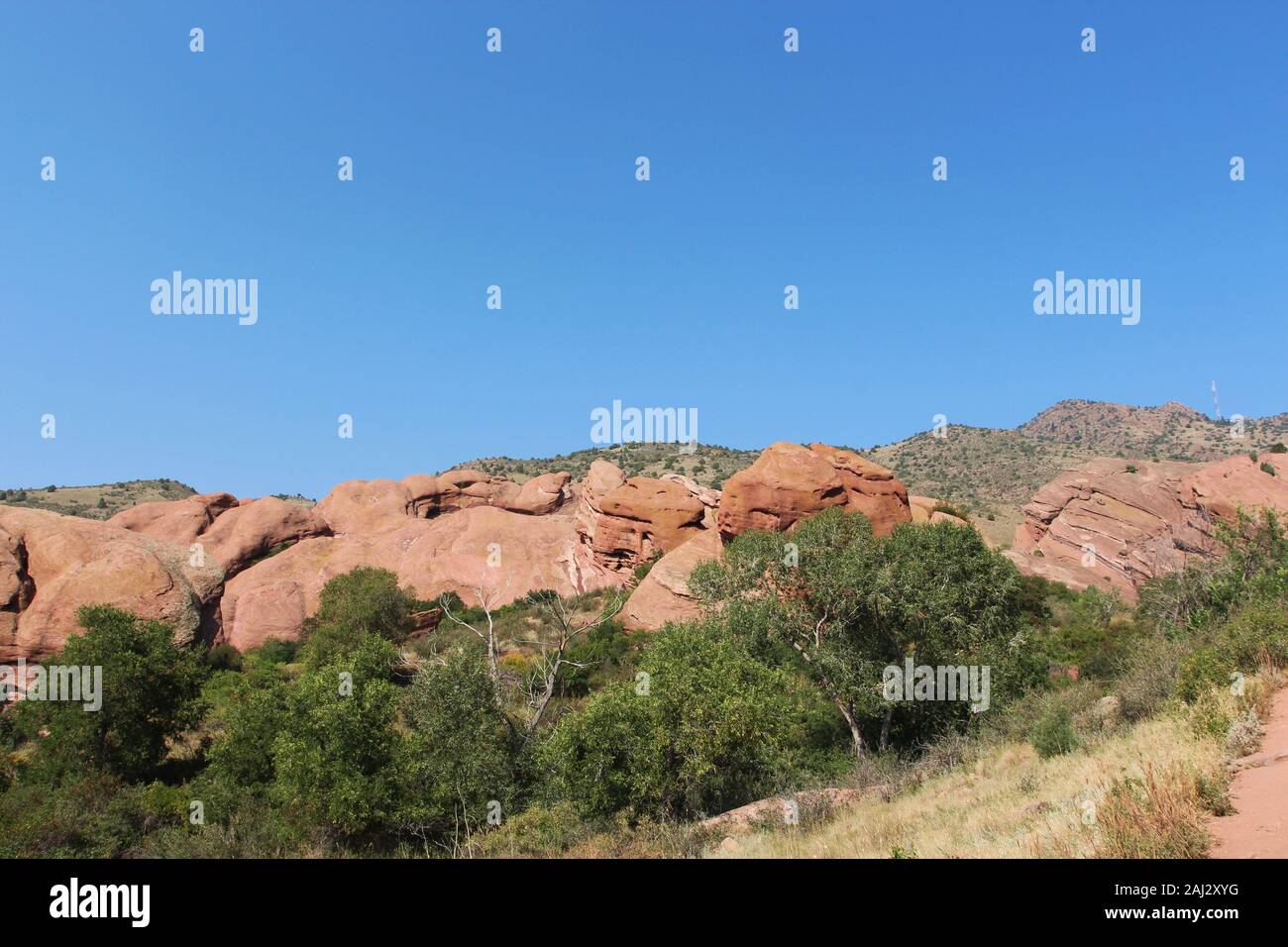 Große rote Felsformationen mit Bäume, Sträucher und Gräser wachsen auf und vor der Formationen auf der Trading Post Trail in Red Rocks State Park, Stockfoto