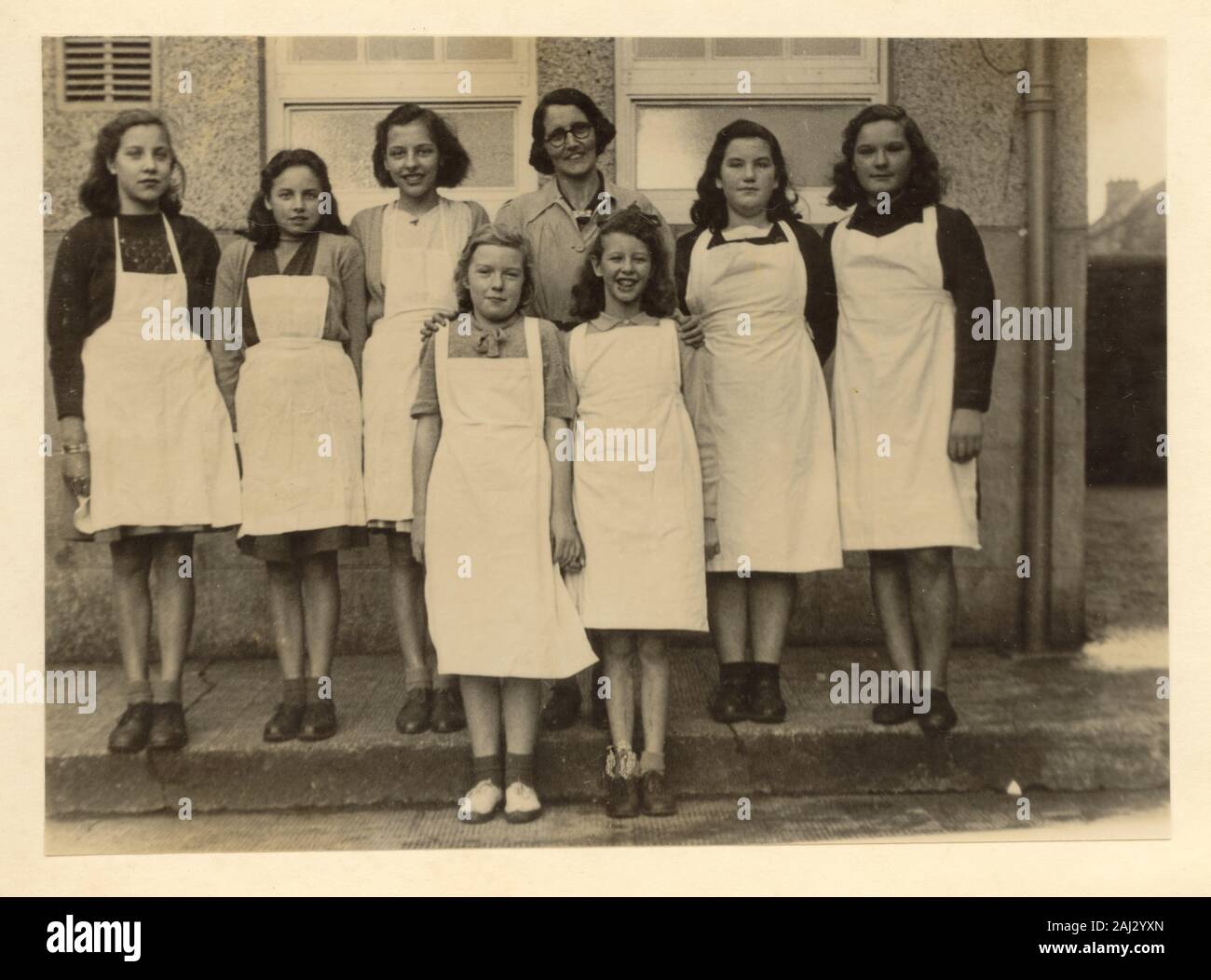 1950 die Schule Mädchen, Schürzen mit ihren inländischen Wissenschaft Lehrer, für ein Gruppenfoto außerhalb ihrer die High School oder Secondary School in Großbritannien posing Stockfoto
