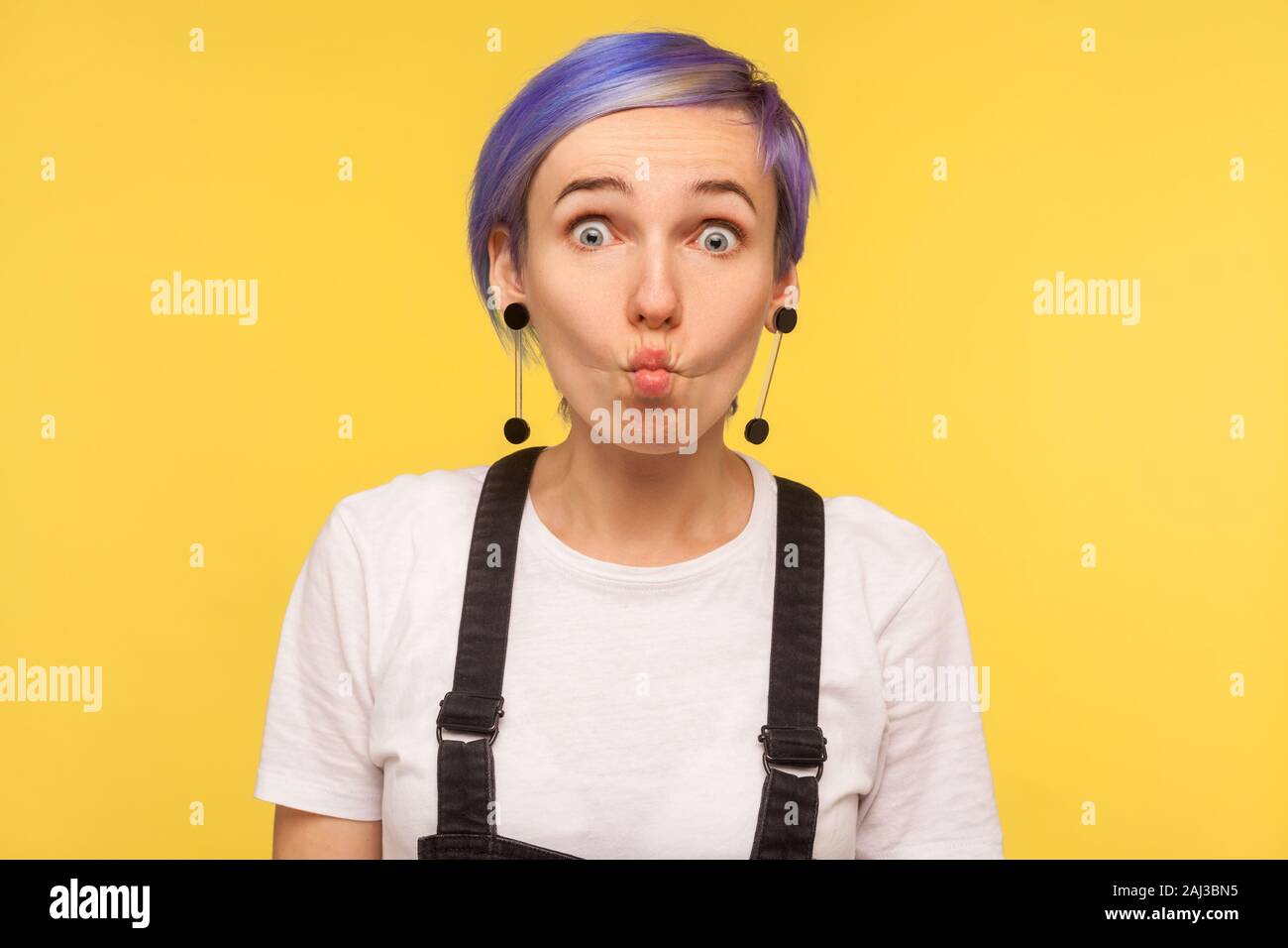 Portrait von Amüsanten hipster Mädchen mit violett kurzes Haar in Jeans Overalls, Fisch Gesicht mit Goofy komischen Ausdruck, dumme Grimasse, Spaß. Ich Stockfoto