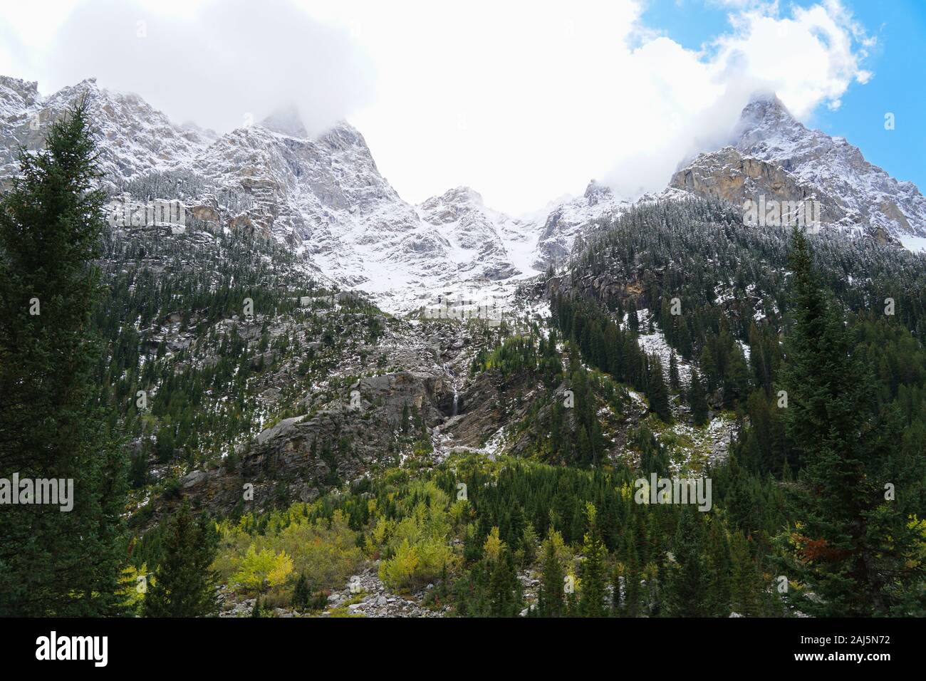 Ein Blick auf die Kaskade Canyon hoch aufragenden Wände mit schneebedeckten Gipfeln, herbstlichen Farben und einem Wasserfall. Stockfoto