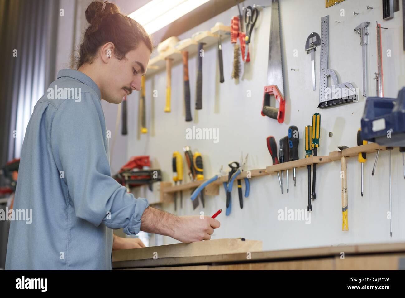 Junge Arbeitnehmer in Freizeitkleidung steht am Tisch und schriftlich etwas mit Arbeit tools auf der Wand in der Werkstatt Stockfoto