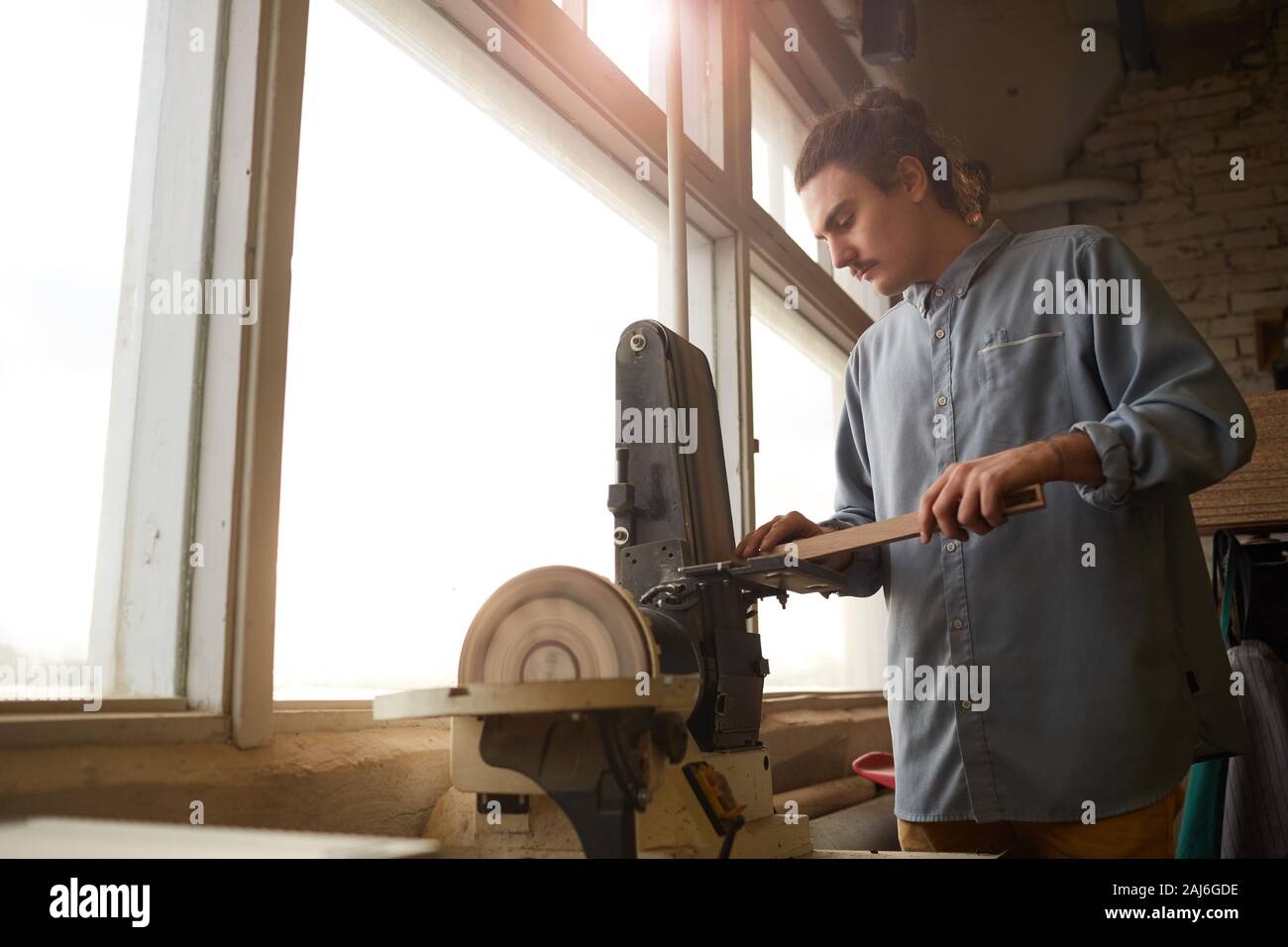 Junge Tischler in Freizeitkleidung stehen und schneiden das Holzbrett mit Drehbank Maschine in der Fabrik arbeiten Stockfoto