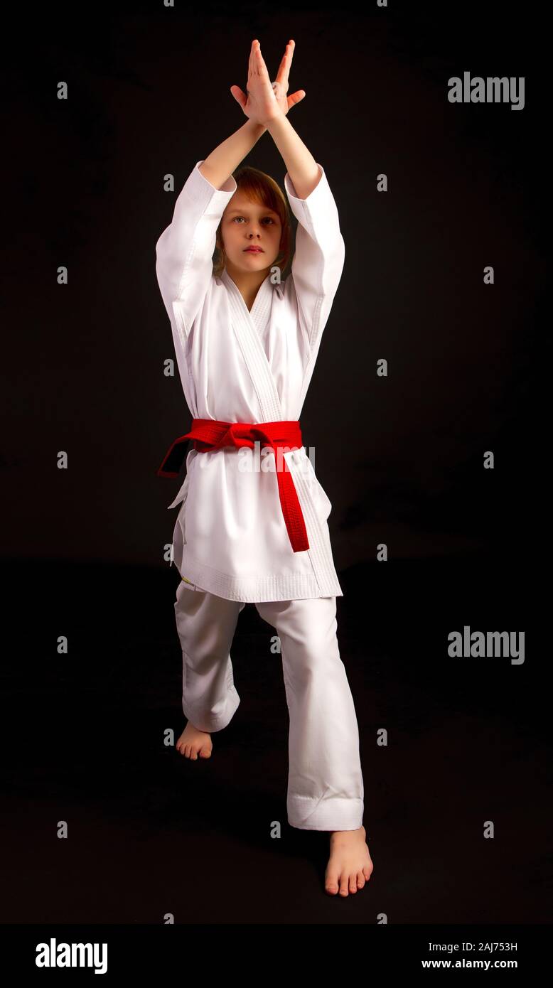 Kleines Mädchen in einem Sport Kimono und einem roten Gürtel führt Übungen in Kata auf einem dunklen Hintergrund Stockfoto
