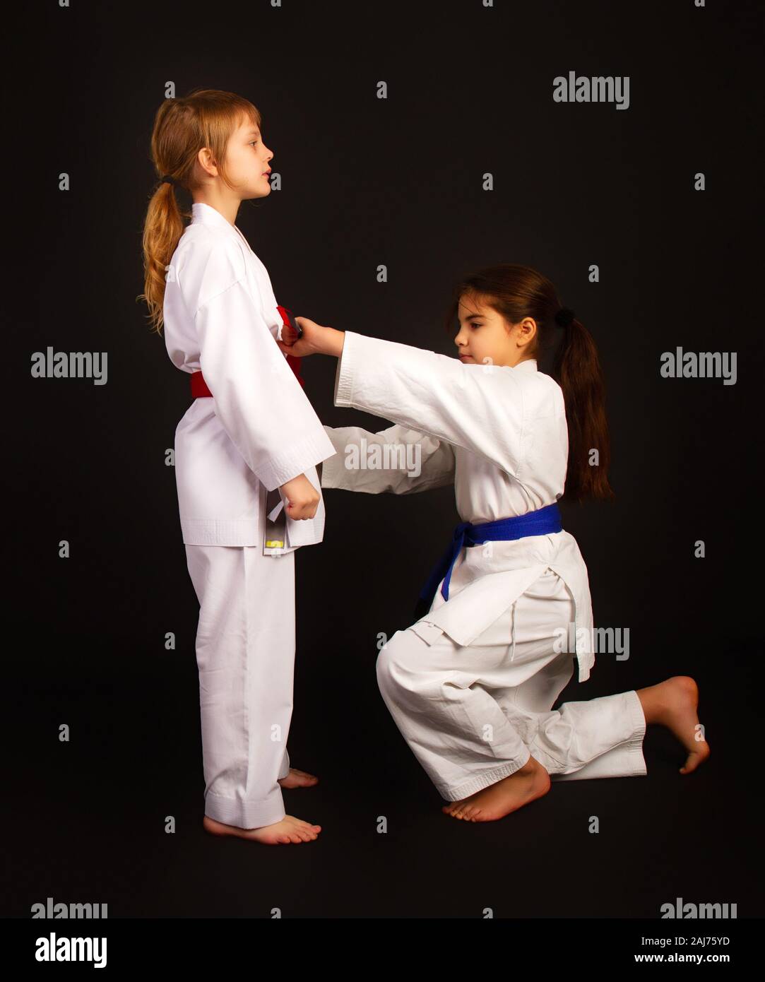Eine weitere erfahrene Karate Mädchen hilft anderen Riegel ein Kimono Riemen korrekt Stockfoto