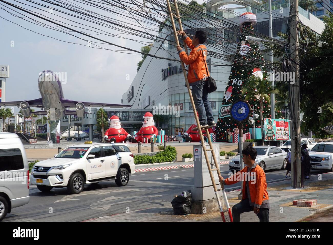 Pattaya, Thailand - Dezember 23, 2019: der Mann, der auf einem Bambus Leiter lehnt sich gegen die power line. Anschlußklemme 21 Shopping Mall auf dem Hintergrund. Stockfoto
