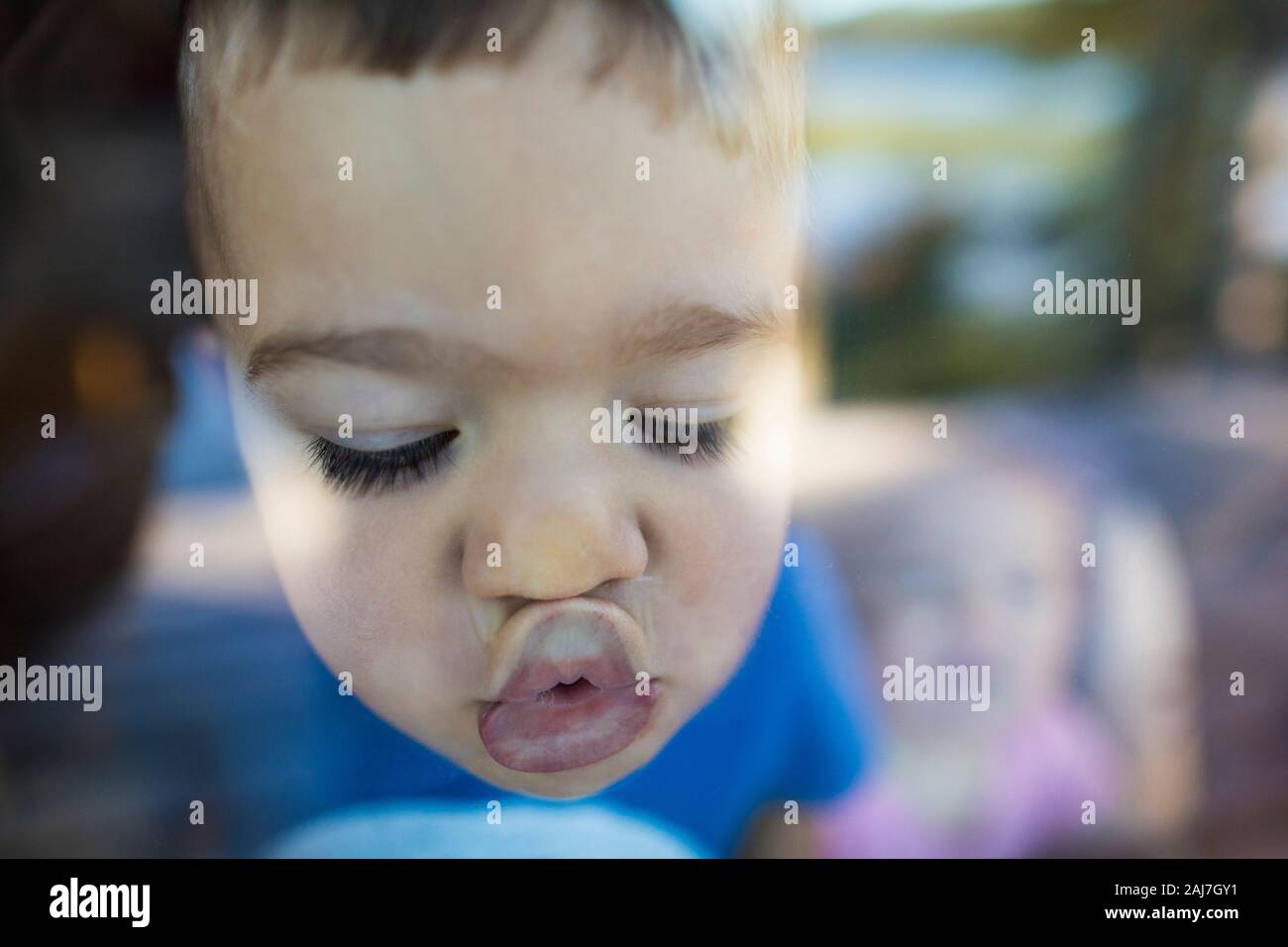 Der junge Junge schiebt seine Lippen gegen ein Fenster, um einen Kuss zu machen Stockfoto