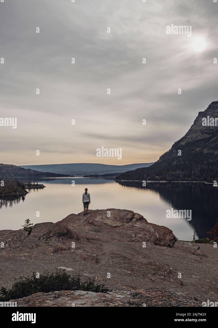 Eineineinige Frau steht vor einem unberührten und ruhigen See in Bergen Stockfoto