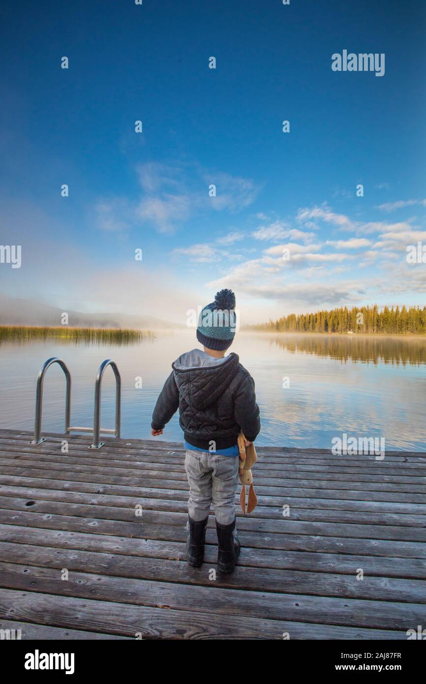 Kleiner Junge, der auf einem Holzsteg am See steht. Stockfoto