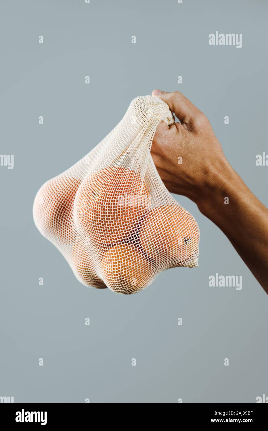 Nahaufnahme von einem Mann mit einem Textilen wiederverwendbaren Netzbeutel, verwendet, um Lebensmittel in loser Schüttung, voll von Orangen, als Maßnahme zur Verringerung der Umweltverschmutzung aus Kunststoff zu kaufen Stockfoto