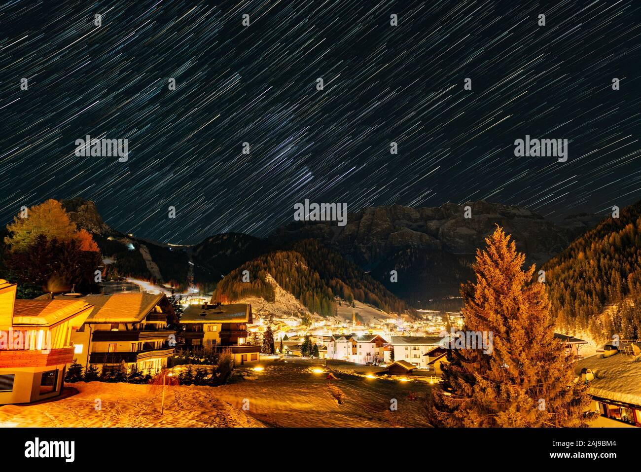 Star Trails über die schneebedeckten Berge und kleinen Dorf Selva di Val Gardena in einer kalten Winternacht Stockfoto