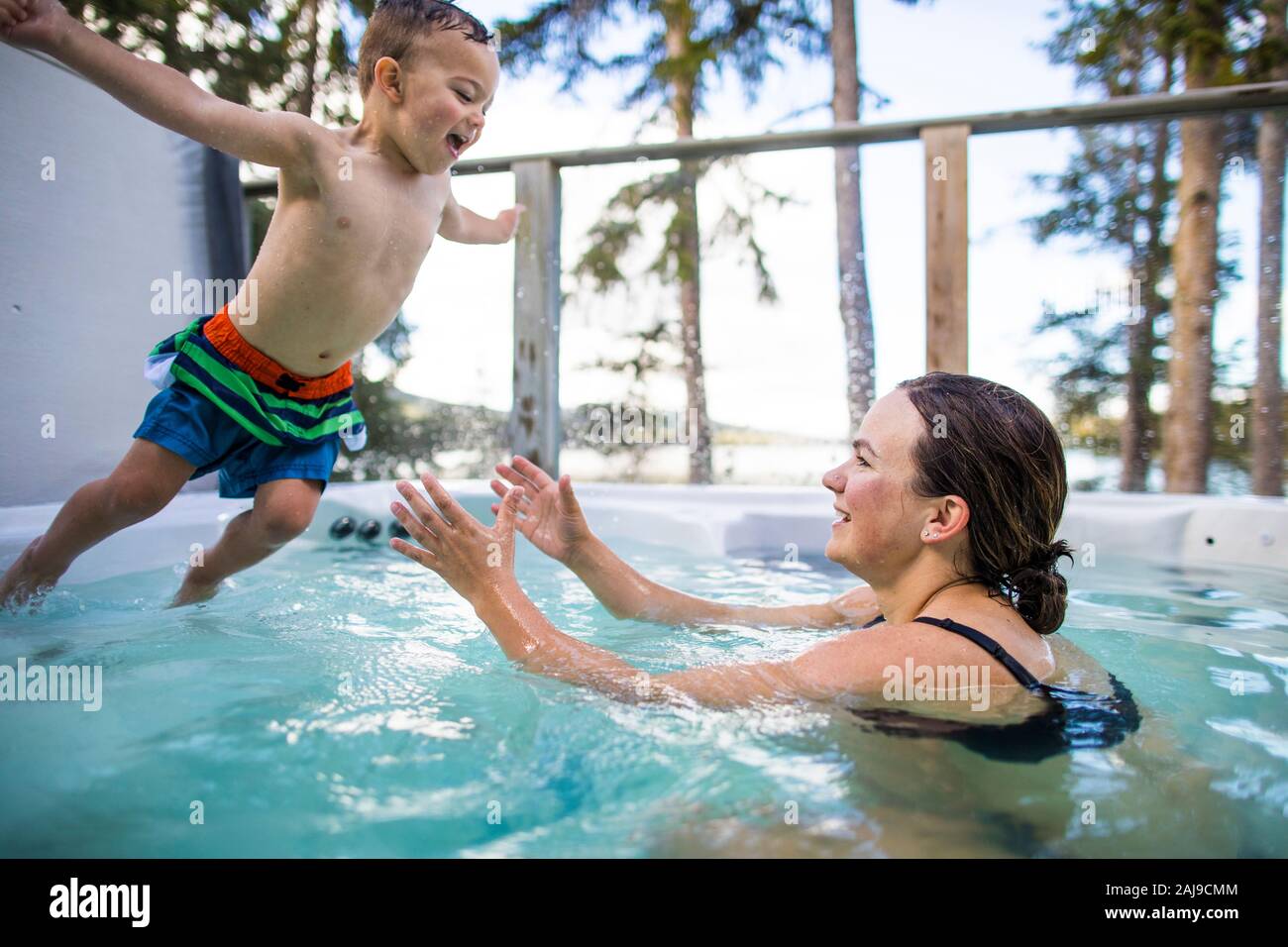 Junger Junge springt in Schwimmbad, Mama wartet, ihn zu fangen. Stockfoto