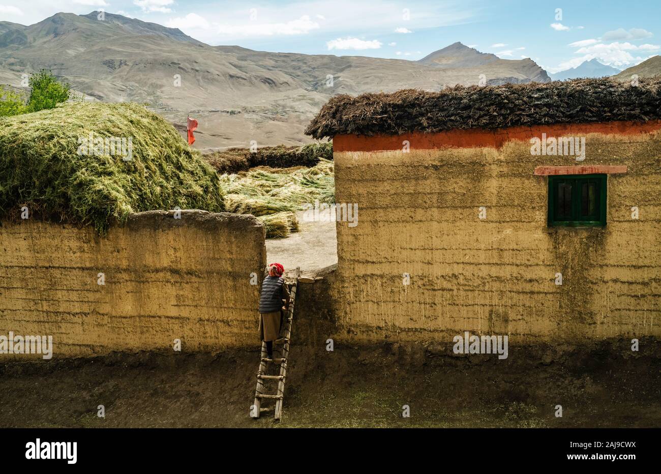 CHICHAM, INDIEN - 16. SEPTEMBER 2019: Traditionelles Haus mit Vieh Trockenfutter auf dem Dach und der Frau mit Blick auf ihre Lager am 16. September 2019 in Chich Stockfoto