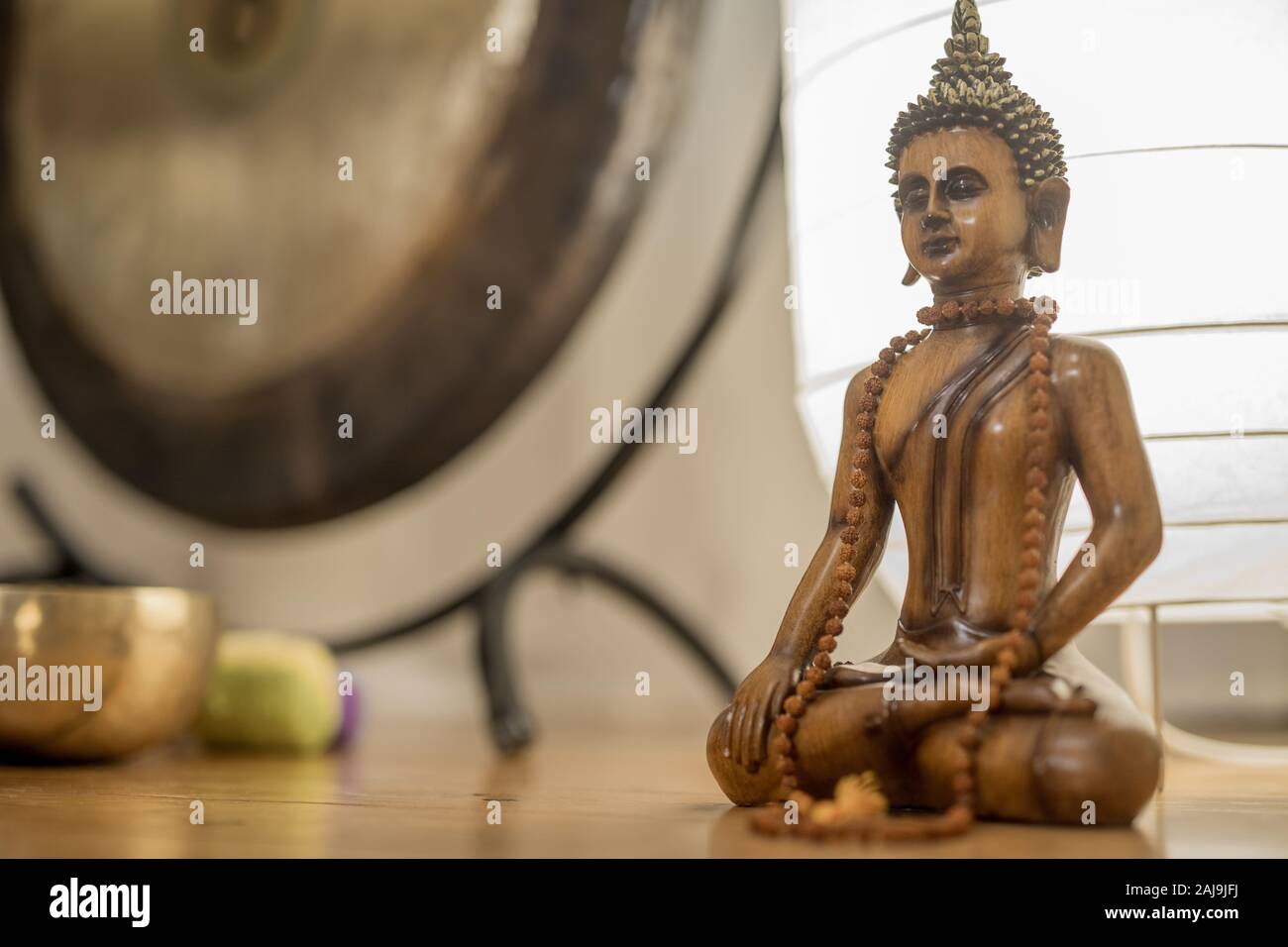 Holz- Buddha Statue in einem Meditationsraum mit Gong und Klangschalen auf dem Hintergrund. Stockfoto