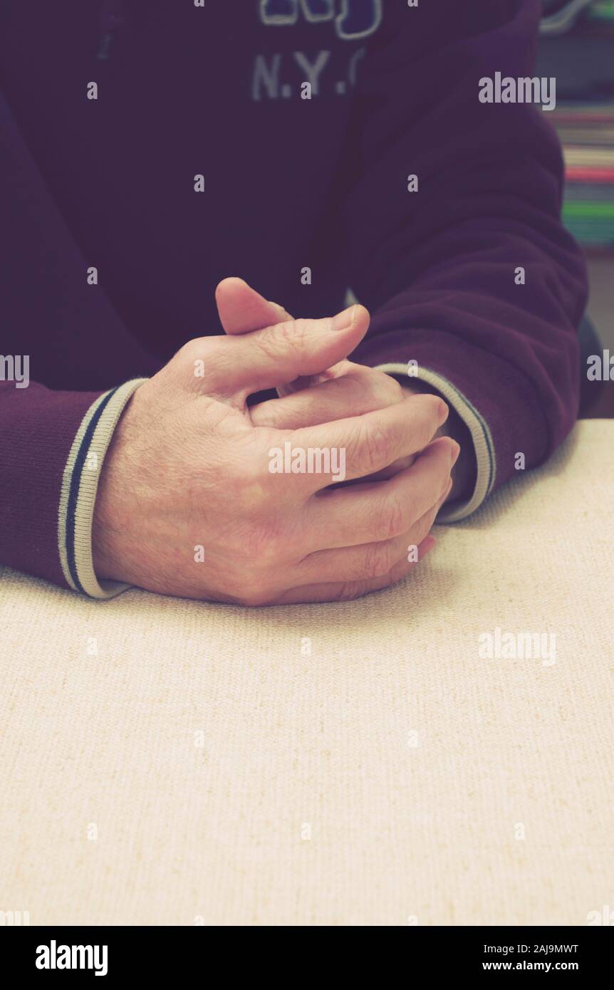 Junger Mann sitzend mit Seiner gefalteten Händen auf dem Tisch Stockfoto