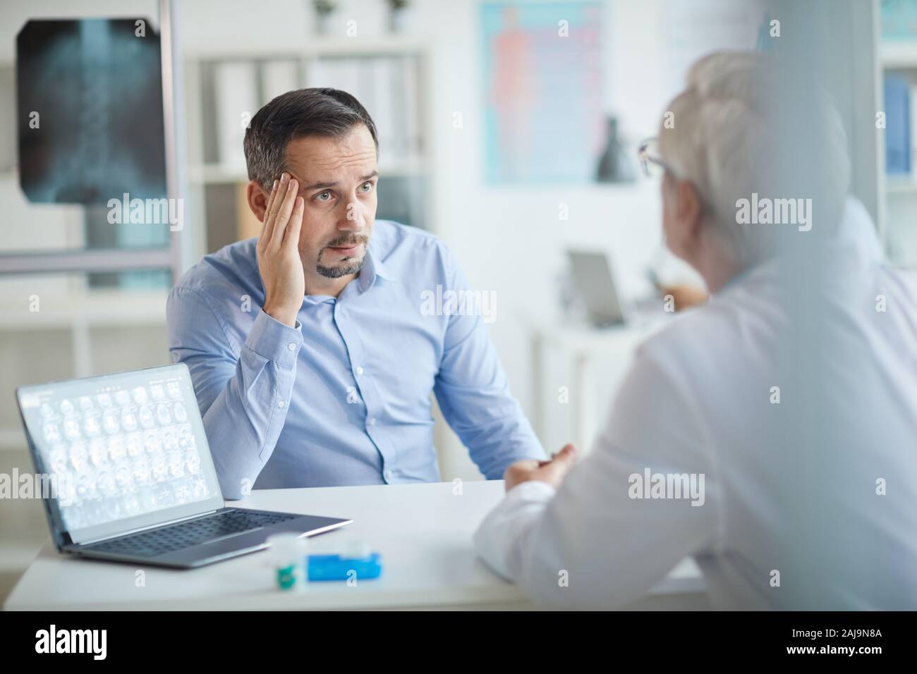 Reifer mann am Tisch sitzen vor dem Arzt und sprechen mit ihm über seine Krankheit bei seinem Besuch im Krankenhaus Stockfoto