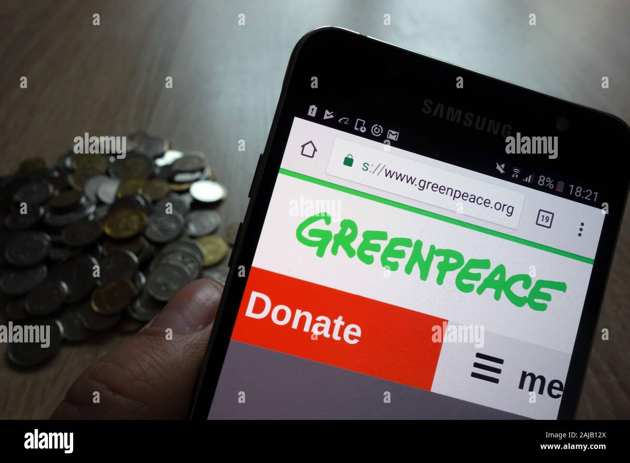 Greenpeace Website auf Samsung Smartphone angezeigt und Stapel von Münzen Stockfoto