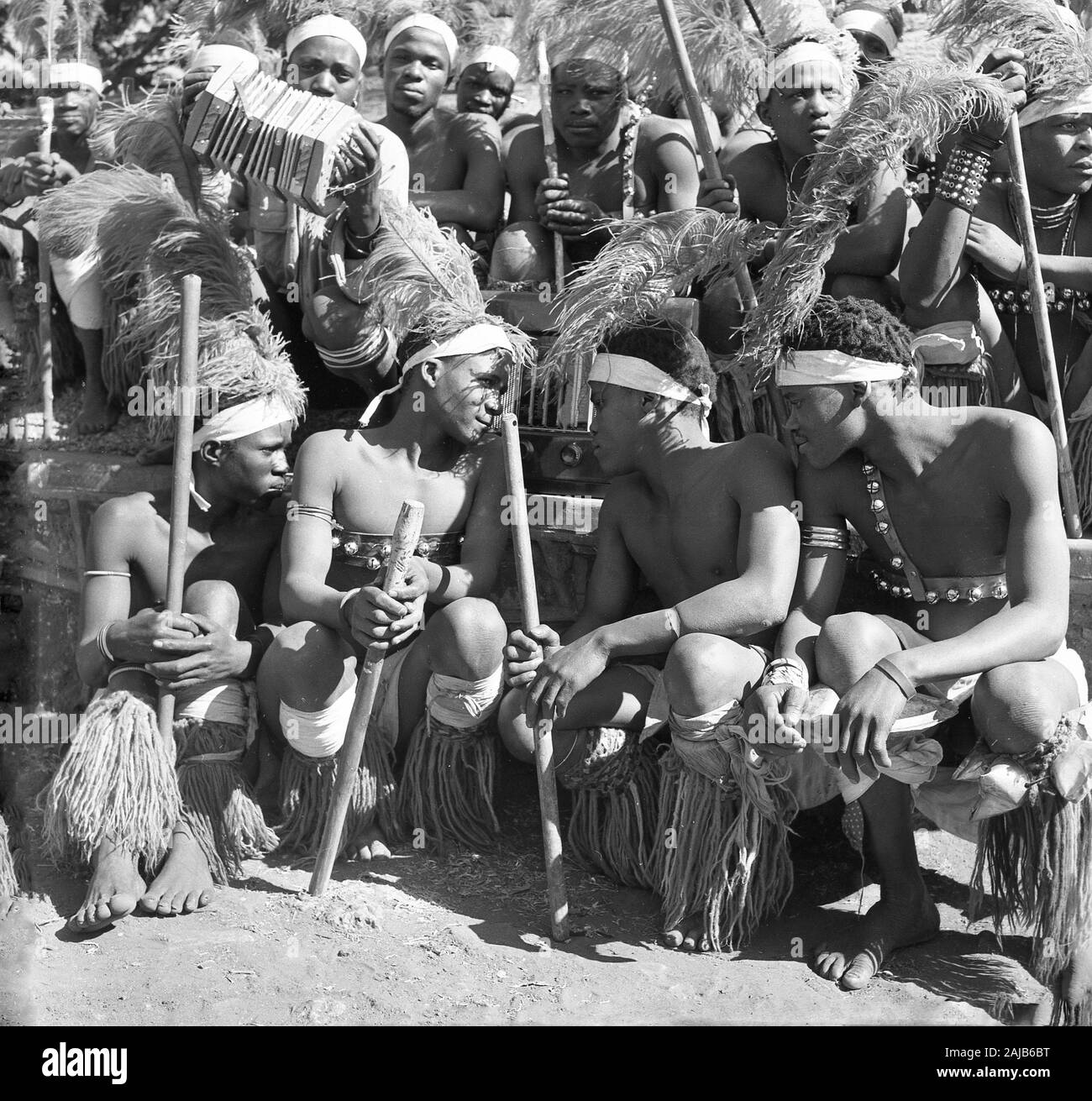Die 1950er Jahre, historisch, eine Gruppe afrikanischer Ureinwohner in traditionellen Stamm- oder Jagdkleiden, die sich zu einem Bild mit einem Briten versammelten, machten Bush Radio, Afrika. Stockfoto