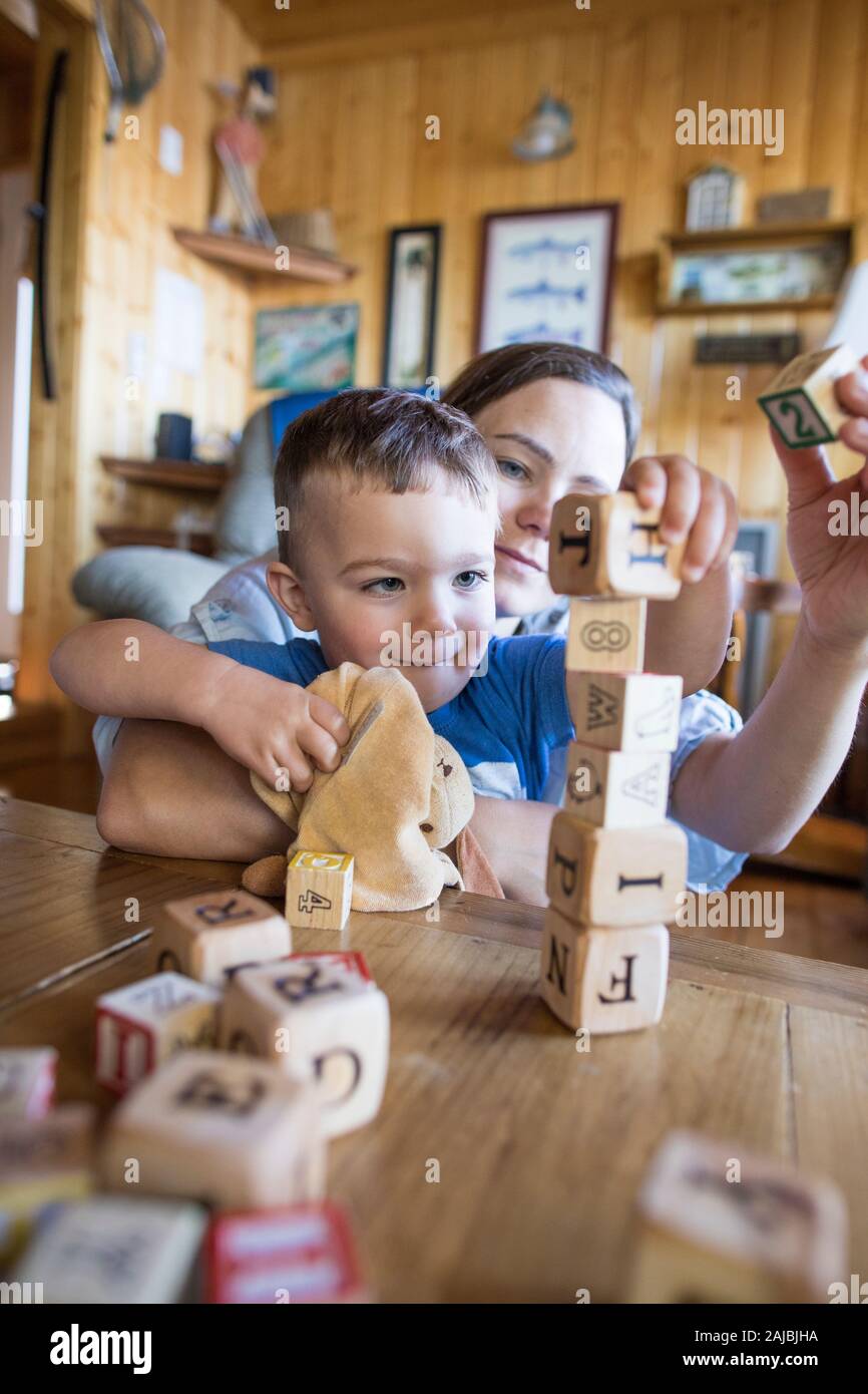 Mutter hilft ihrem Sohn, aus Holzblöcken einen hohen Turm zu bauen. Stockfoto