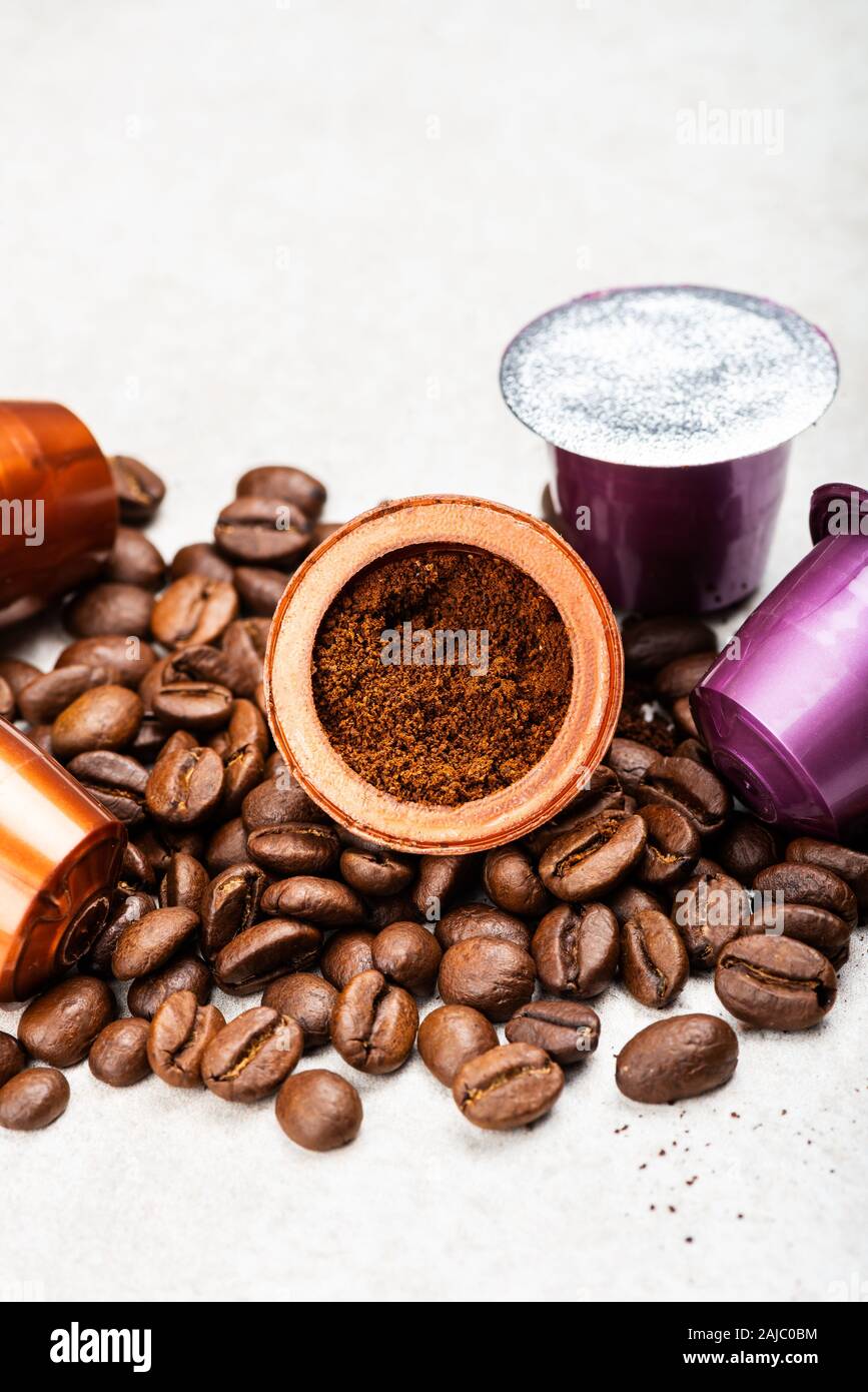 Öffnen Espresso Kaffee Kapseln mit geerdetem drinnen Kaffee und gerösteten Kaffeebohnen auf grauem Hintergrund Stockfoto