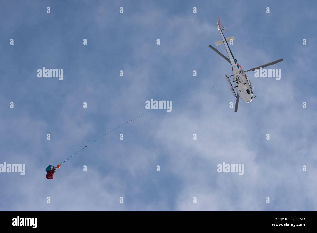 Eine tragende Hubschrauber blau, bewölkter Himmel. Cargo ausgesetzt auf ein langes Seil. Stockfoto