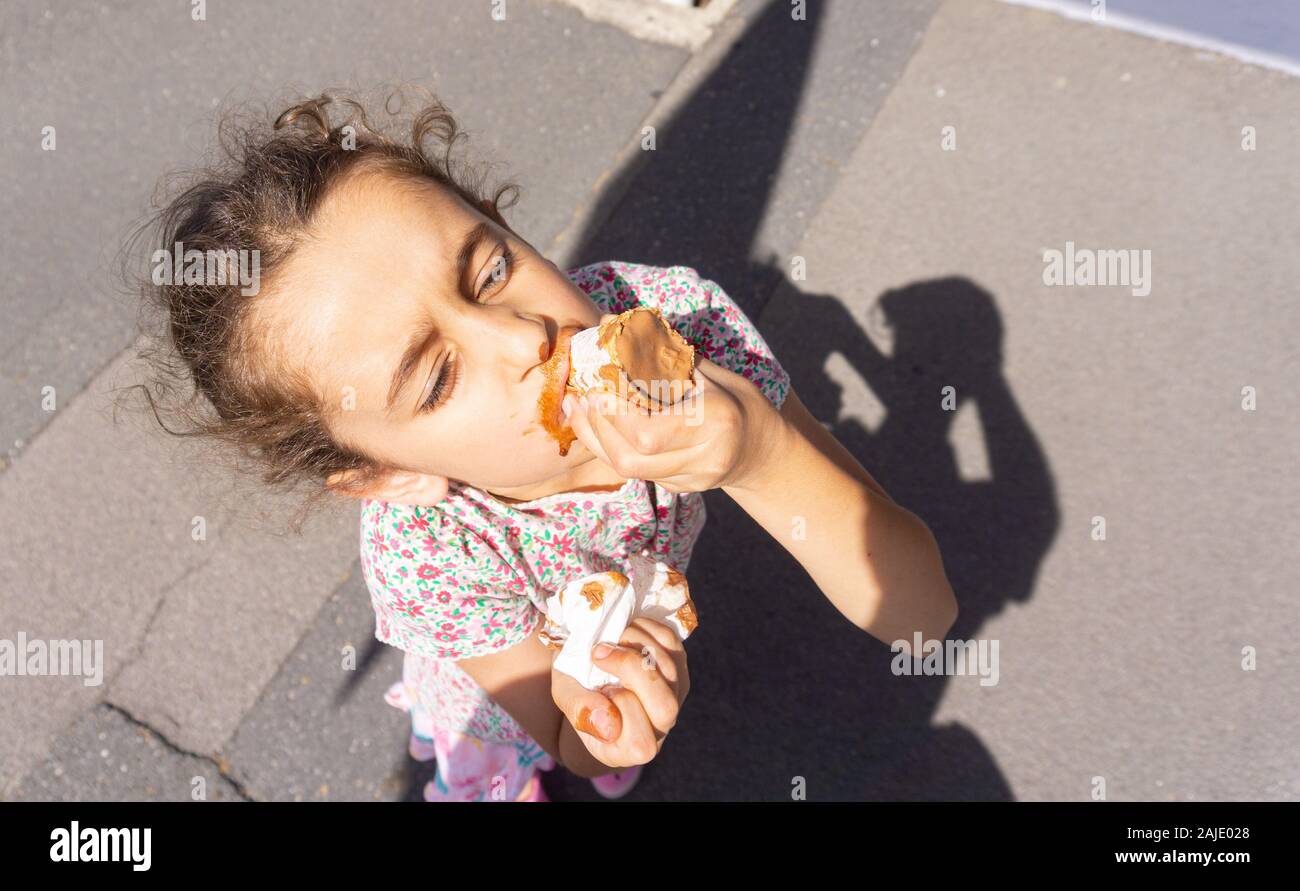 Kleines Mädchen mit unordentlichen Gesicht genießen saugen Schokolade Eis von der Unterseite des Kegels in Stadt Straße. Stockfoto