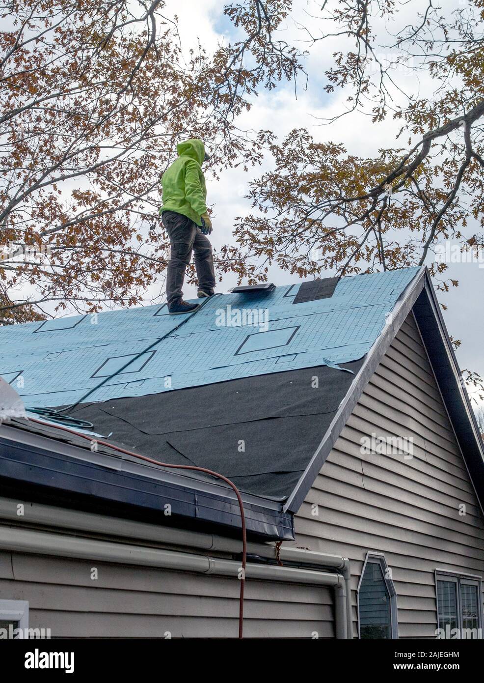 Ein Arbeiter steht auf dem Dach eines Hauses, das immer Neue teerpappe und Schindeln Stockfoto