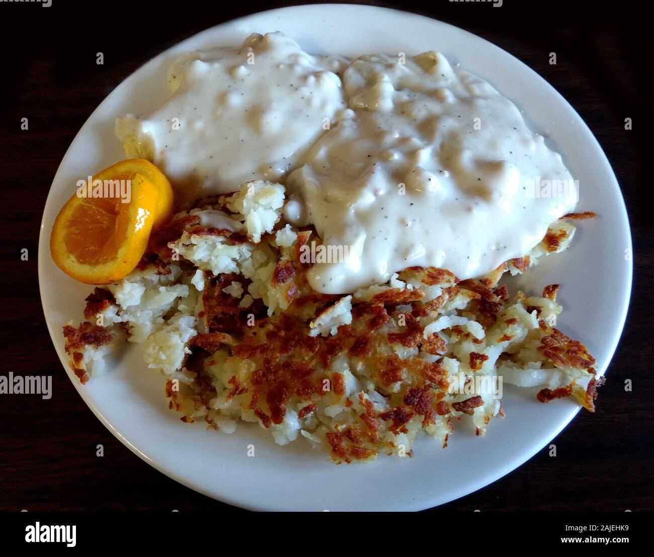 Herzhafte wurst Soße über flauschige Kekse serviert und mit knusprigen Bratkartoffeln und eine Orange Slice gekoppelt Stockfoto