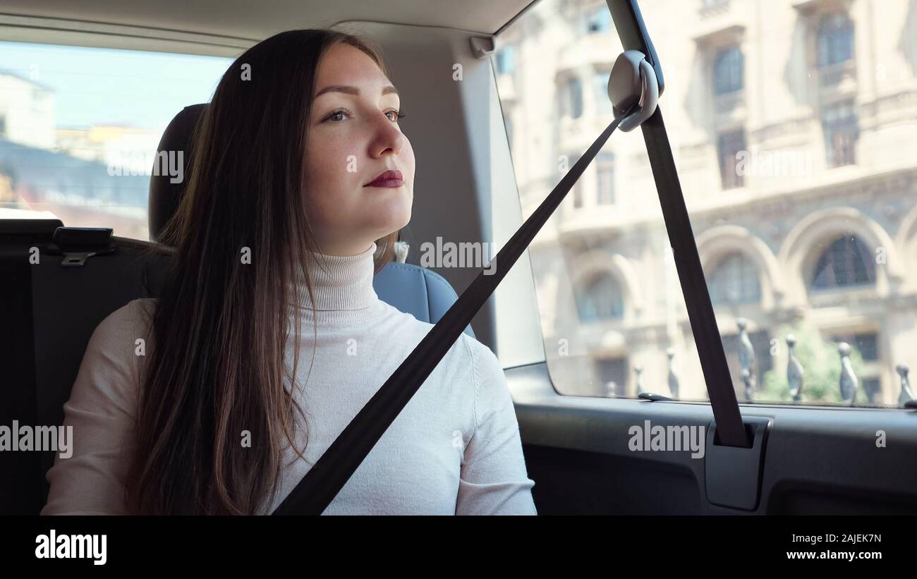 Anmutige Dame mit dunklen roten Lippen sitzt im Auto warten auf Treiber gegen architektonische Gebäude außerhalb Fenster closeup Stockfoto