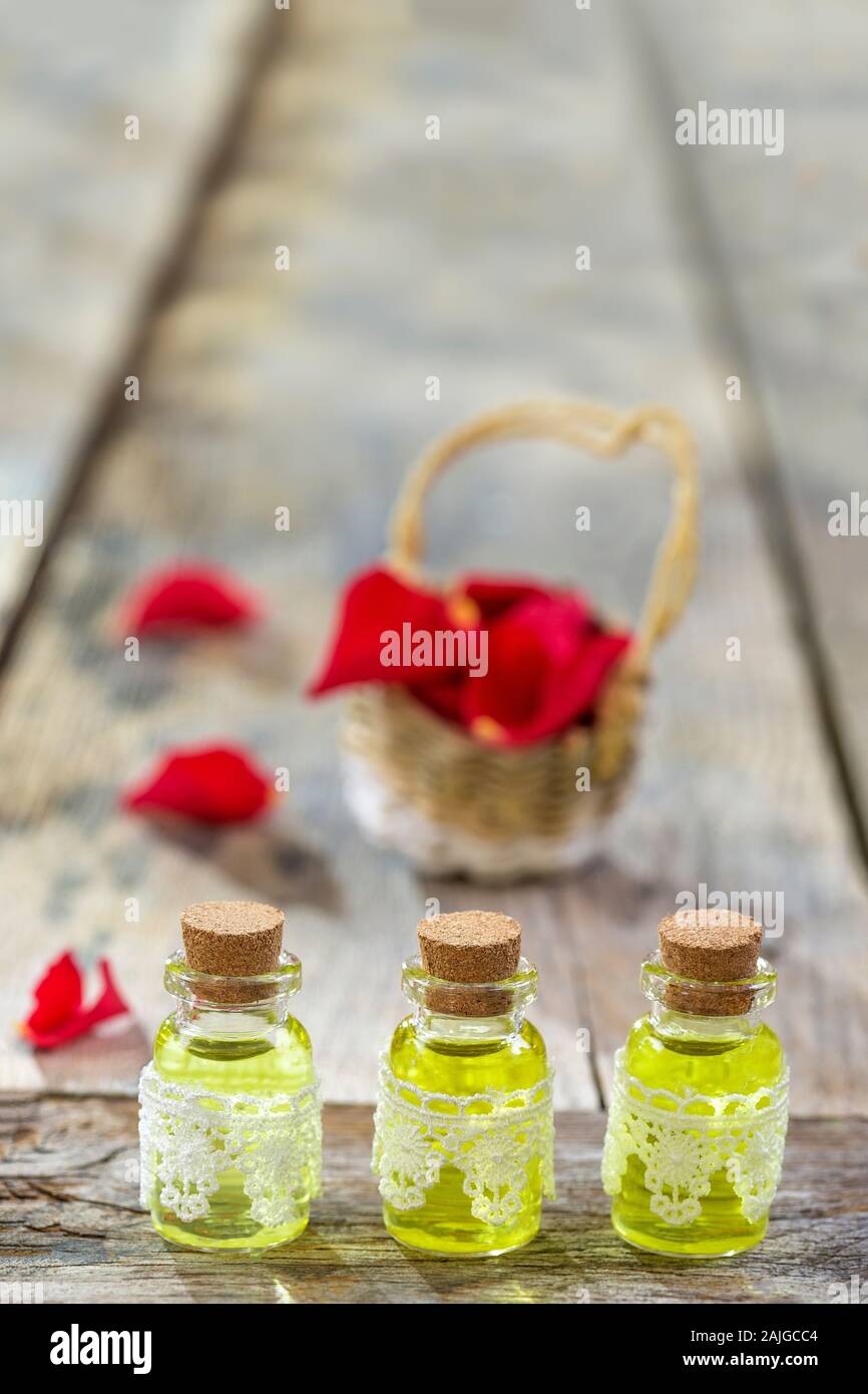Rustikale Weidenkorb mit roten Rosen Blütenblätter hip Blumen und Flaschen wesentliche Rosen öl. Holz- Hintergrund, kopieren, Stockfoto