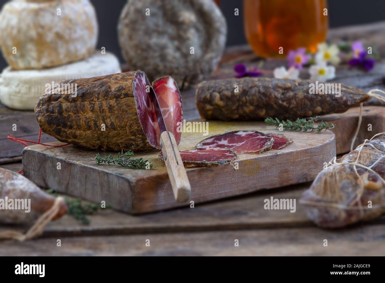 Mehrere traditionelle korsische Wurst mit einem Olivenzweig und schwarzen Oliven auf Holz- Hintergrund. Stockfoto