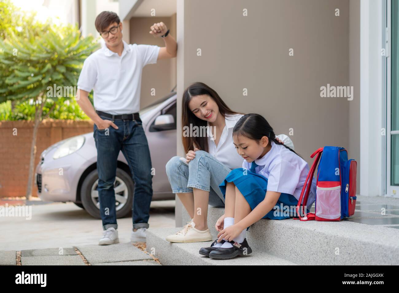 Asiatische Familie mit Vater, Mutter ihre Tochter Vorschulkinder Fernsehen in Uniform zu Ihren eigenen Schuhen infront von zu Hause für die Schule vorzubereiten Stockfoto