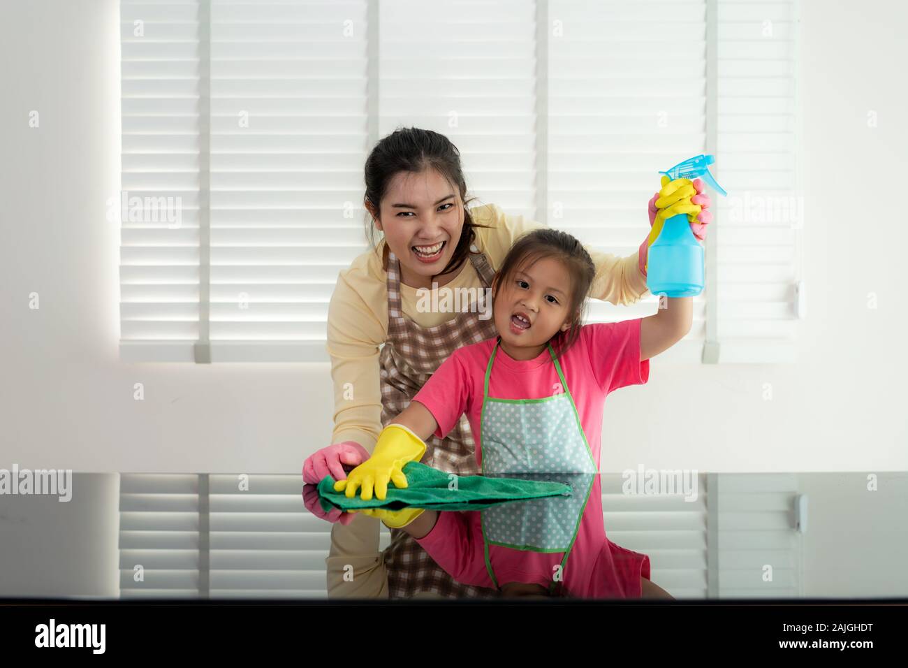 Asiatische fröhliche Mutter und Tochter Reinigung der Oberfläche mit rag und Sprühflasche zusammen und Waffen für eine erfolgreiche Reinigung Haus angehoben. Happy fami Stockfoto