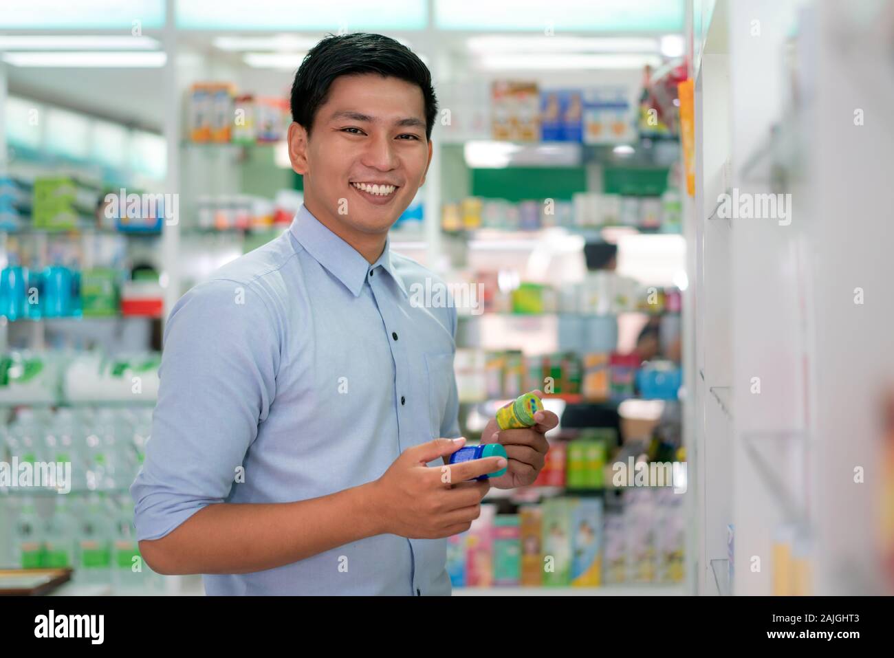 Asiatische stattlichen Kunden mit einem reizenden Lächeln Sie Produkt und Kamera in der Apotheke und Drogerie. Medizin, Pharmazie, Gesundheit Stockfoto