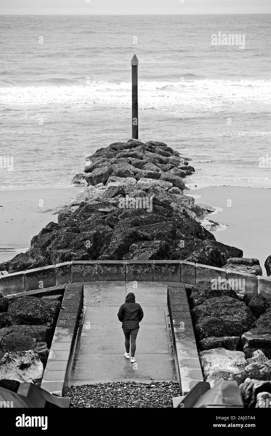 Person in Blau zu Fuß entlang der konkrete Brücke von einer künstlichen Wellenbrecher auf rossall Strand, Fleetwood Stockfoto