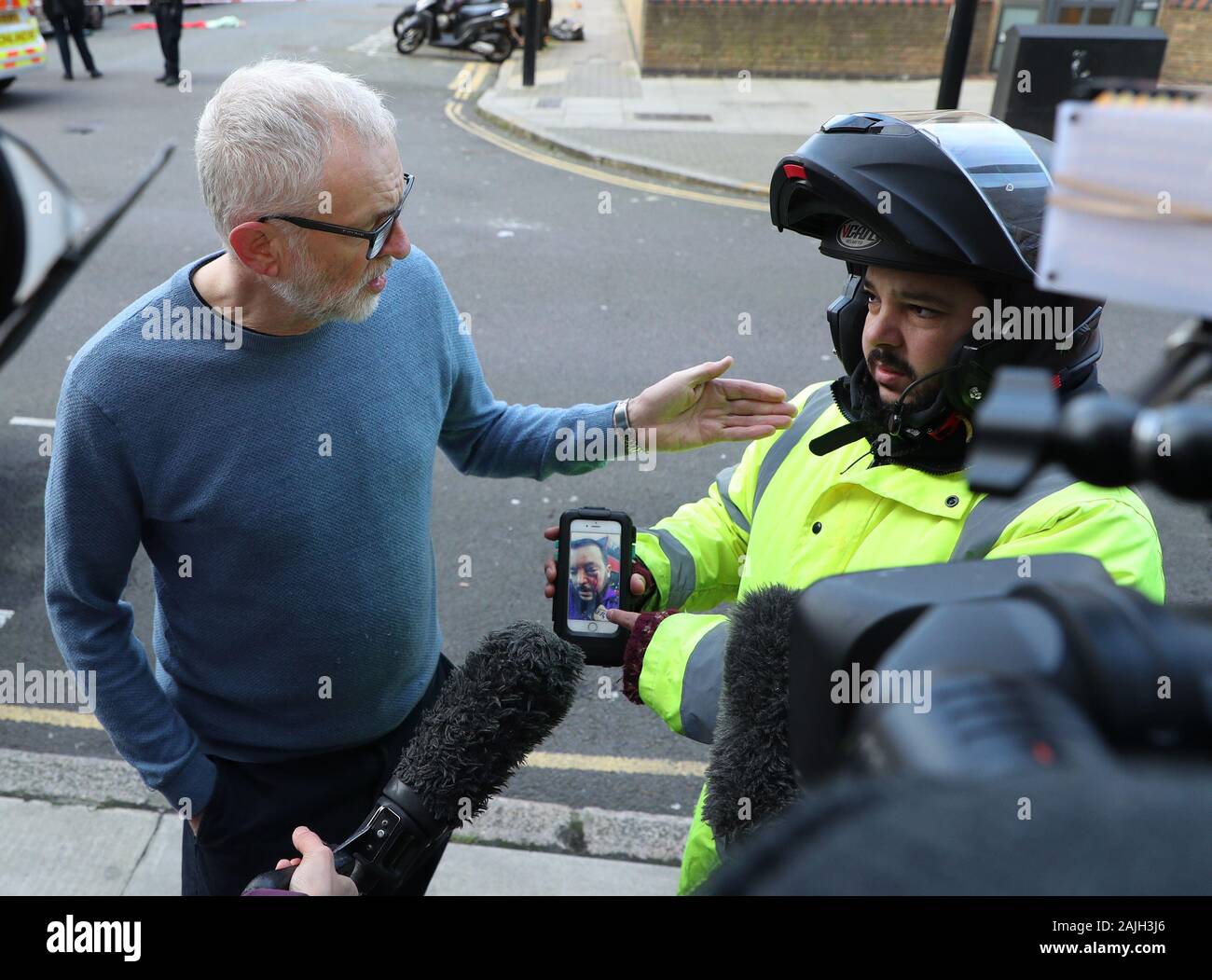 Deliveroo rider Zakaria Gherabi, im Alter von 37, zeigt der Führer der Jeremy Corbyn ein Foto auf seinem Mobiltelefon an seinen schweren Verletzungen, nachdem er in der Vergangenheit angegriffen zu werden, während eine Medien Interview an der Szene von charteris Straße nahe der Kreuzung mit der Lennox Straße in Finsbury Park, nachdem ein Mann wurde zum Tod im Norden Londons erstochen am Freitag Abend. Stockfoto