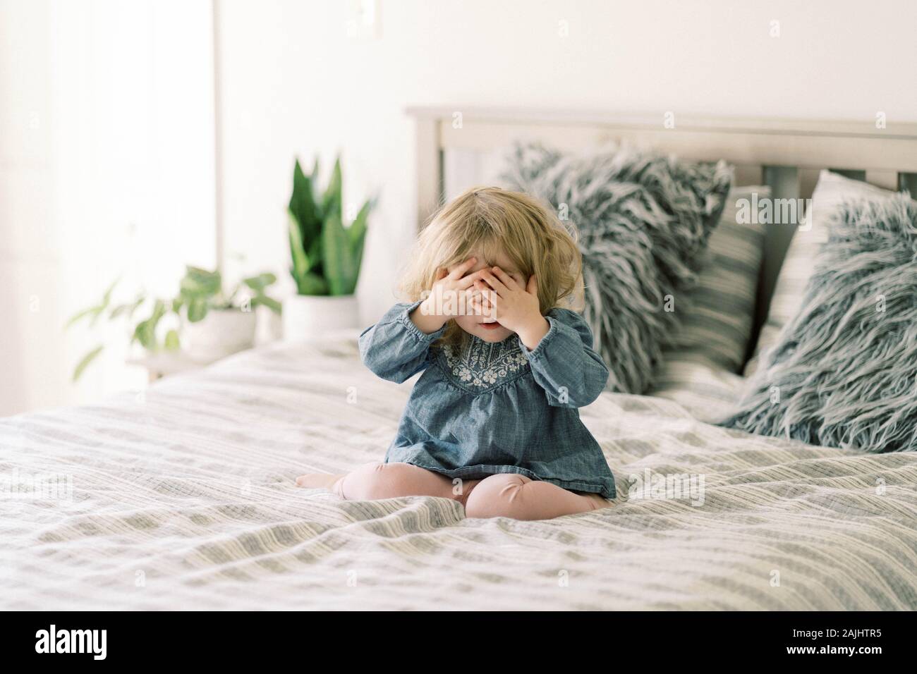 Kleines Kleinkind Mädchen spielt Peek-a-boo auf dem Bett ihrer Eltern. Stockfoto