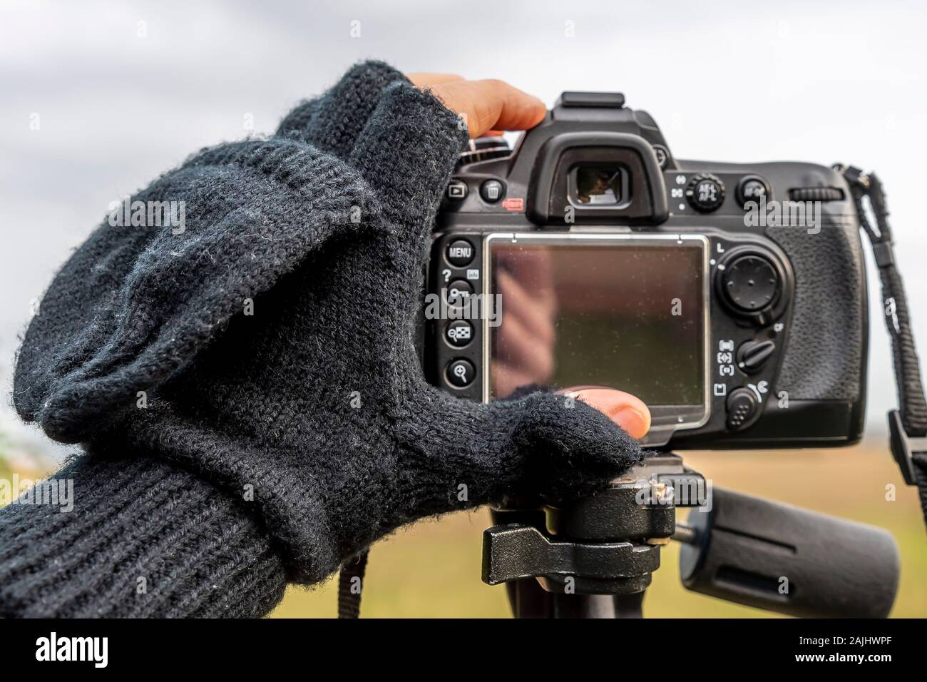 Eine Hand in einem wollenen Handschuhe fallen, nur mit den Fingerspitzen aufgedeckt stellt eine Kamera auf einem Stativ in der Wintersaison Stockfoto