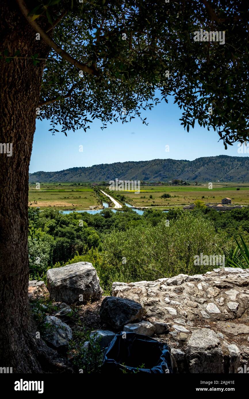 Hohen Winkel sonniger Frühlingstag Blick auf Lagune Salz See, das Tal und die Berge im Nationalpark von Butrint in Albanien, Europa. Verschwommen Stein fort Wände und Einstreu in den Vordergrund. Stockfoto