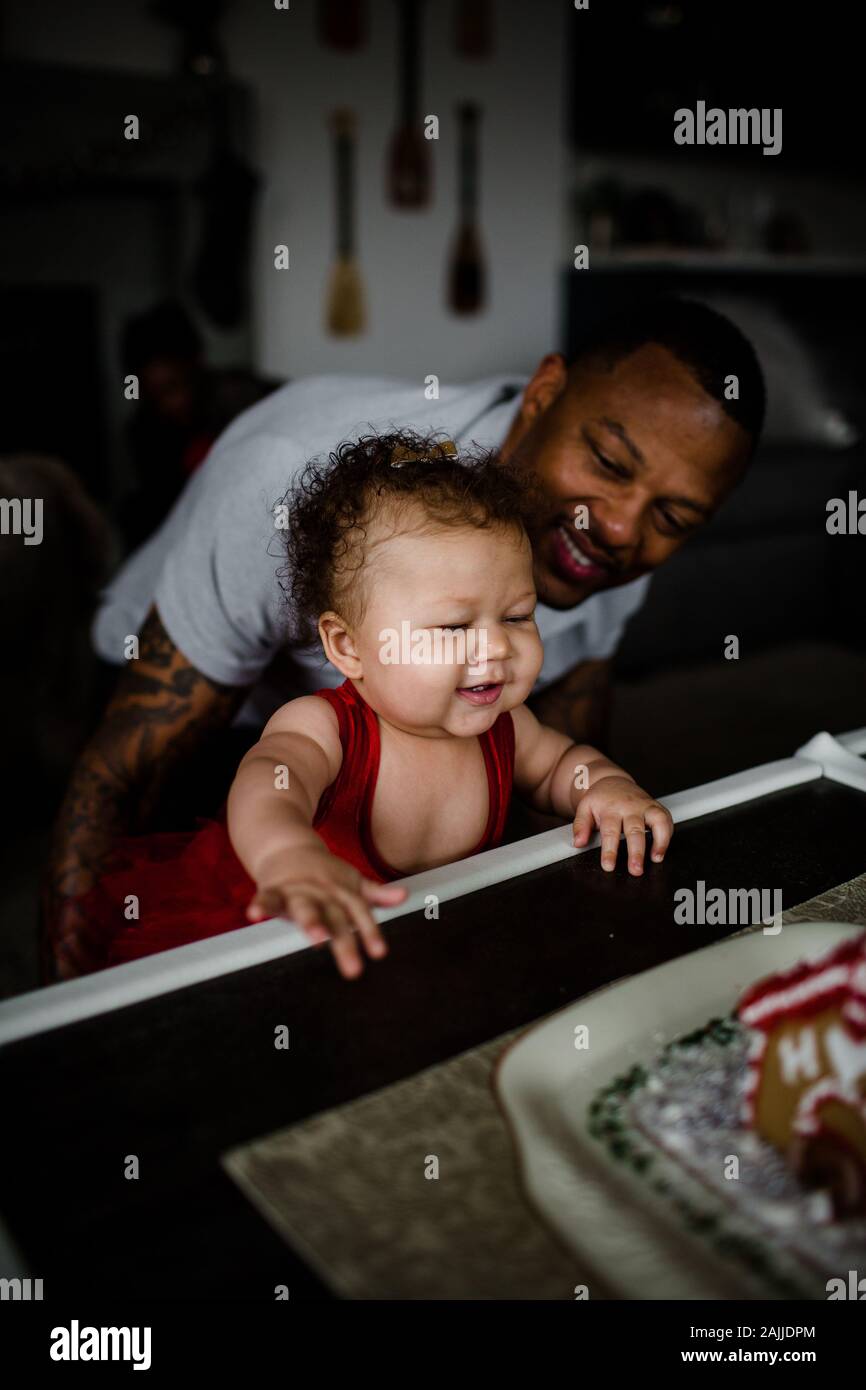 Mixed Race Baby zieht sich selbst an den Tisch, als Papa anschaut Stockfoto