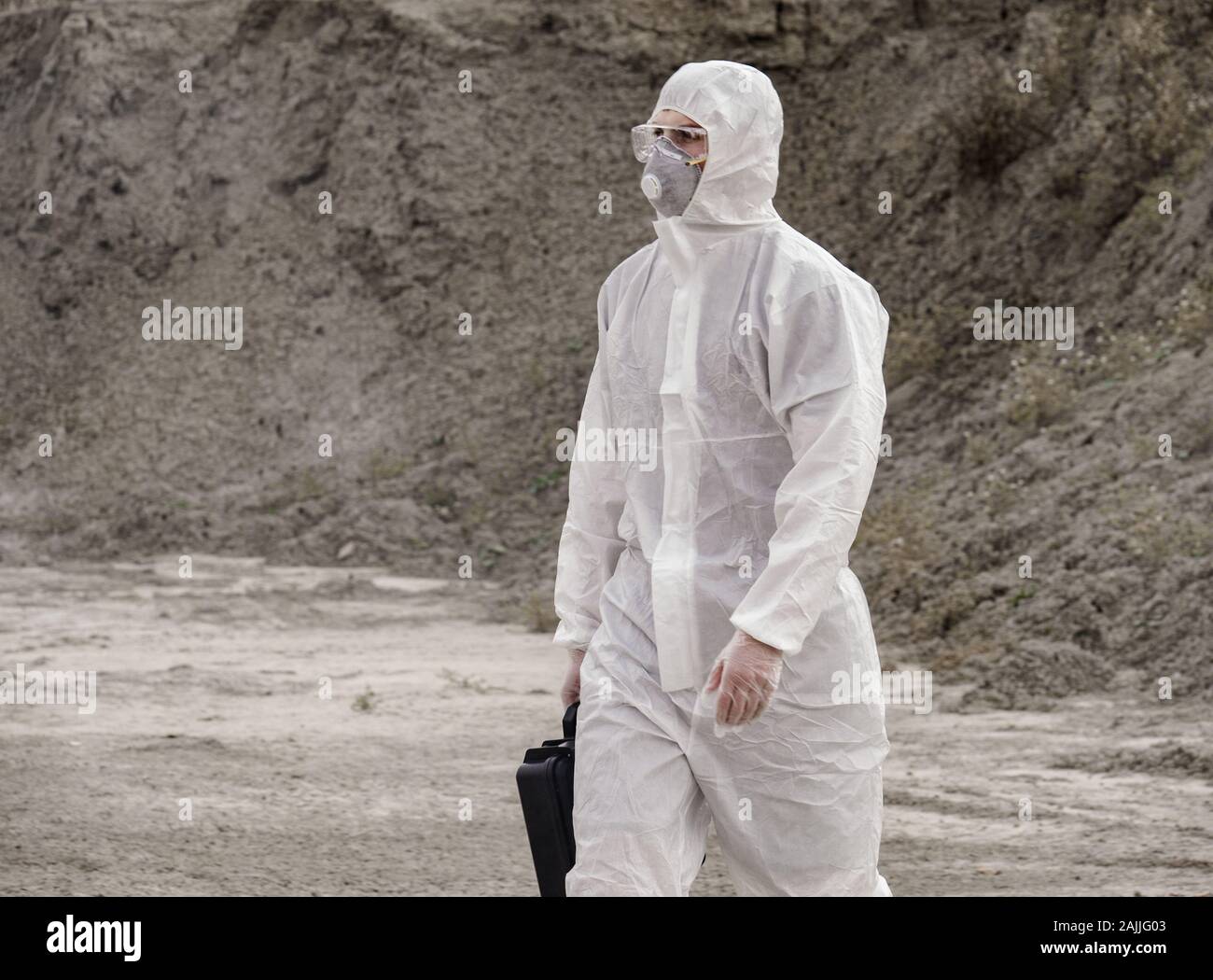 Lab Techniker in einer Maske und Schutzanzug gegen Chemikalien, Spaziergänge auf trockenem Boden mit einem tool box durch giftigen Rauch Stockfoto