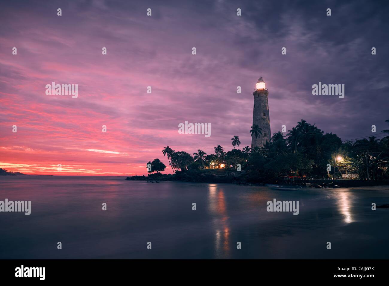 Beleuchtete Leuchtturm in der Mitte von Palmen gegen dramatische Himmel. Südküste von Sri Lanka an Bunte sunrise. Stockfoto