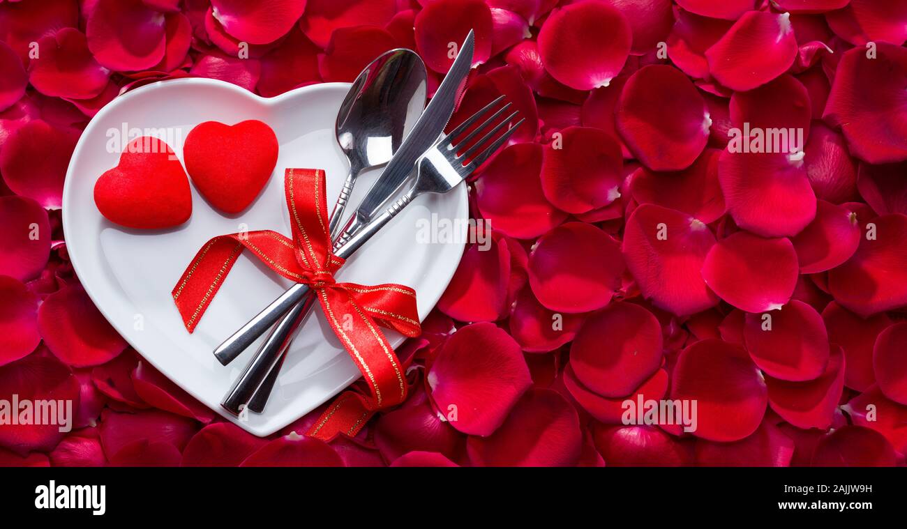 Rosenblätter auf herzförmige Platte mit Messer und Gabel, Valentines Tag essen Hintergrund Stockfoto