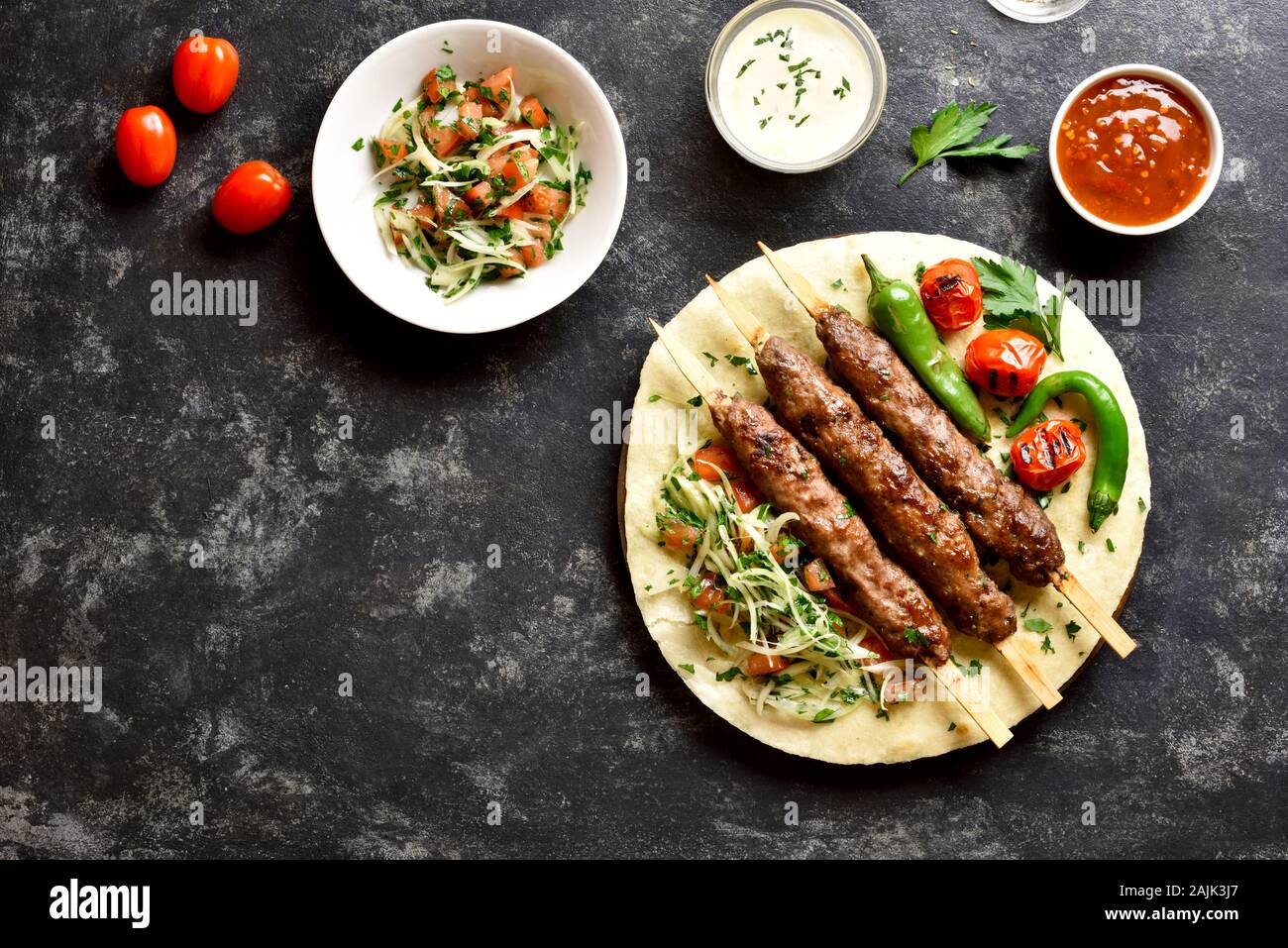 Türkische Adana Kebab mit frischem Gemüse auf Fladenbrot und Soße über schwarzen Stein Hintergrund. Ansicht von oben, flach Stockfoto