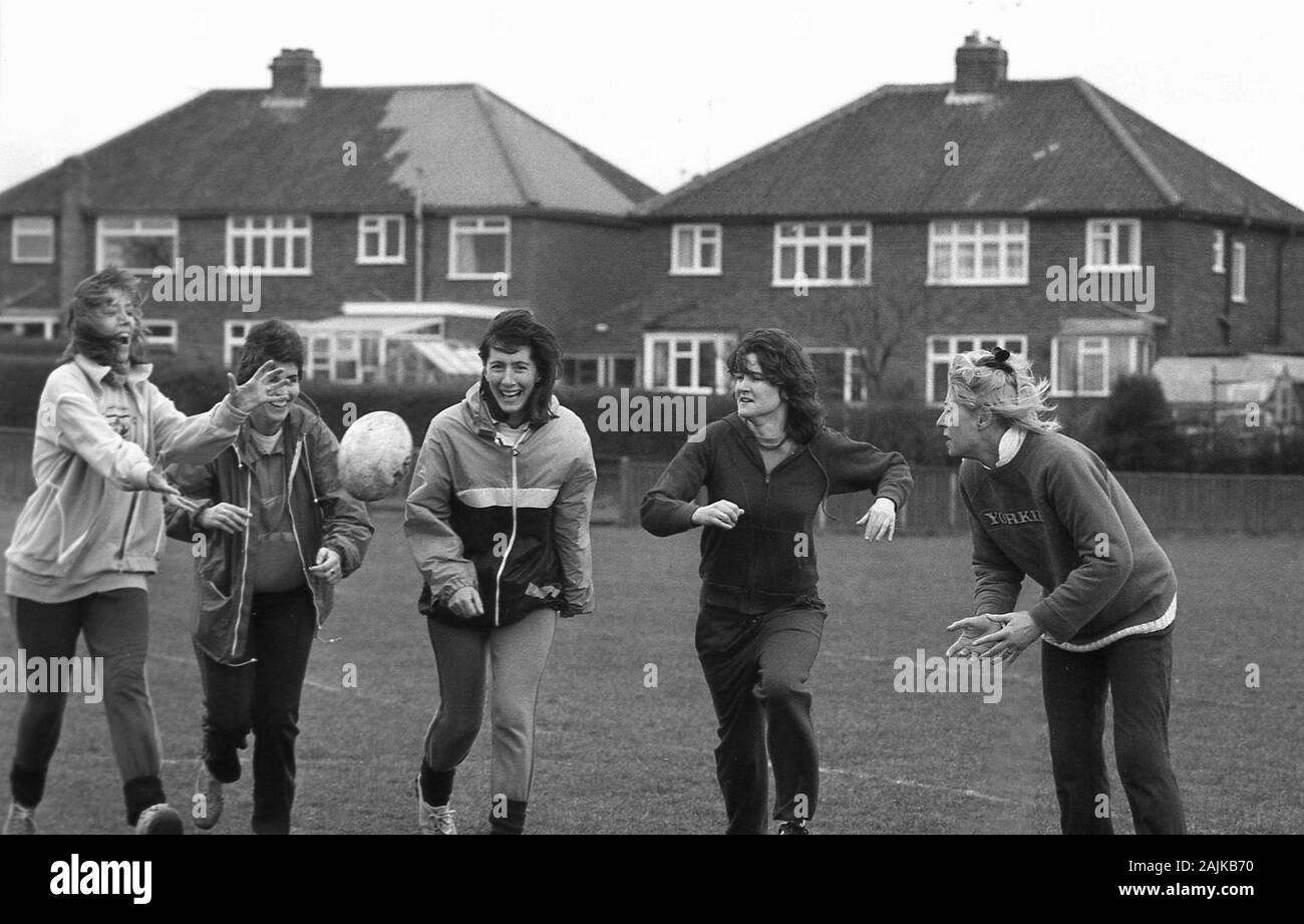 1980er Jahre, historische, weibliche Schullehrer im PE-Kit außerhalb eines Sportplatzes mit Spaß und körperlicher Bewegung, mit einem Rugbyball spielen, England, Großbritannien. Stockfoto