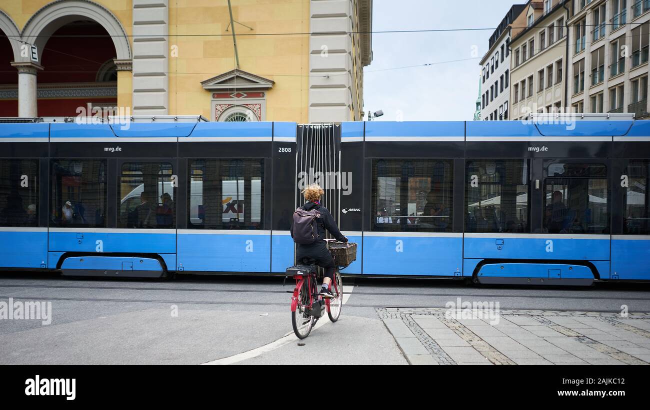 Straßenszene im historischen Innenstadtkern Münchens mit weiblicher Radfahrerin, die auf eine Straßenbahn wartet, bevor sie weitergeht. Stockfoto