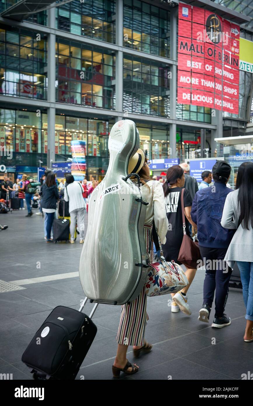 Musikerin trägt ihr Cello in coolem Silberkoffer durch die geschäftigen Menschenmassen am Berliner Hauptbahnhof. Stockfoto