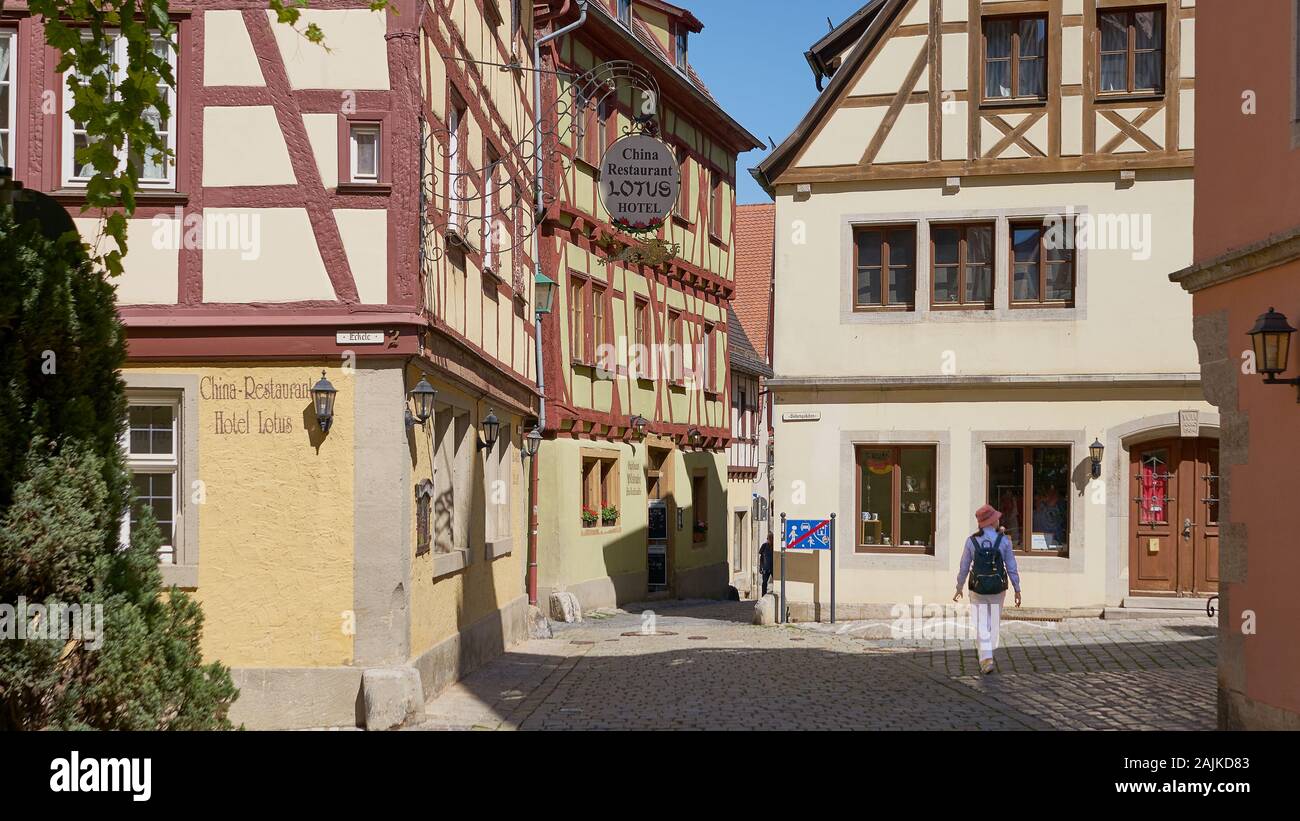 Einsame weibliche Touristin spaziert durch die leerstehenden mittelalterlichen Straßen Rothenburgs mit schönen Fachwerkhäusern. Stockfoto