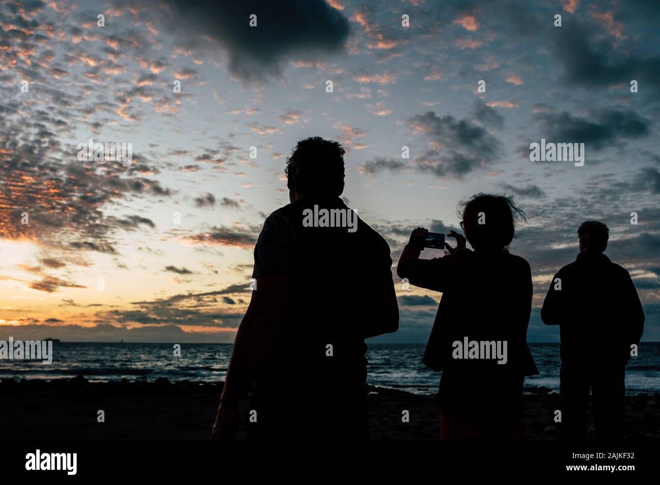 Menschen in Silhouette genießen und mit Handy am wunderschönen Sonnenuntergang am Strand - Begriff der Freunde und gemeinsam Urlaub - touri Stockfoto